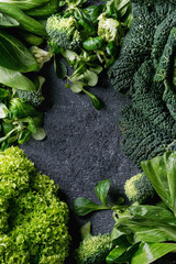 Variété de salades de légumes verts crus, laitue, bok choy, maïs, brocoli, chou de Milan comme cadre sur fond de texture de pierre noire. Vue de dessus, espace pour le texte
