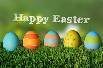 Inscription Happy Easter and painted colorful eggs in the grass.
