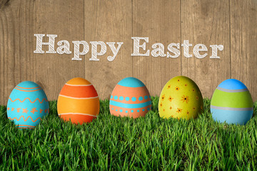 Inscription Happy Easter and painted colorful eggs in the grass.