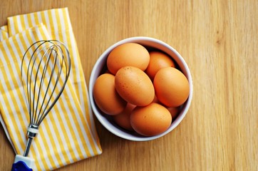 Bowl of hen eggs with whisk on napkin on a rustic wooden background ready for preparing breakfast...