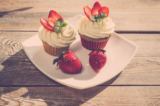 Fresh tasty cupcake with strawberry and leaves of mint on wooden backgroundwith. Retro tone