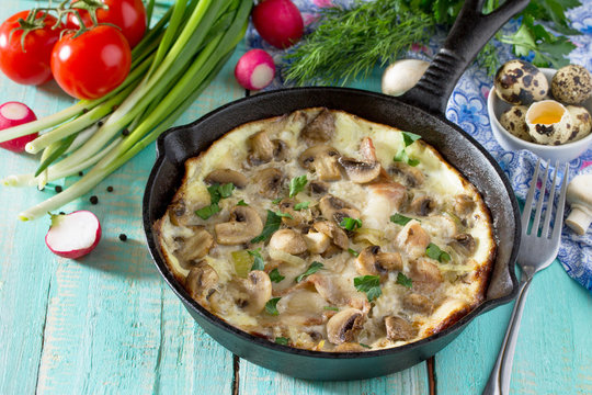 Omelette from quail eggs with ham and bacon in a cast iron frying pan on a wooden table. The concept of healthy nutrition and diet.