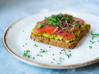 Homemade toasts with avocado and smoked salmon, sprinkled with cress and black sesame on the white plate