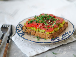 Homemade toasts with avocado and smoked salmon, sprinkled with cress and black sesame on the white plate
