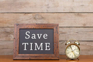 Alarm clock and blackboard with text "Save time"" on brown wooden background