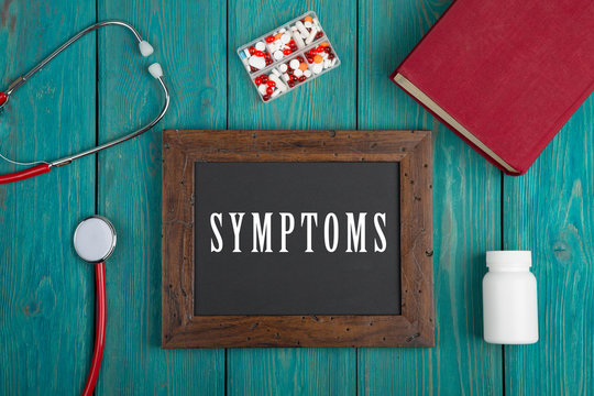 Blackboard with text "Symptoms", book, pills and stethoscope on blue wooden background