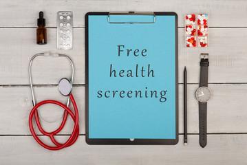clipboard with text "Free health screening", pills, watch and stethoscope