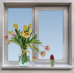 Easter. Window. A bouquet of yellow tulips in a three liter jar and an Easter egg on a windowsill.