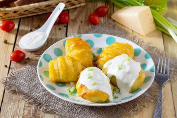 Baked potato with cheese served with cream sauce and greens on a wooden table in a rustic style.