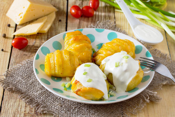 Baked potato with cheese served with cream sauce and greens on a wooden table in a rustic style.