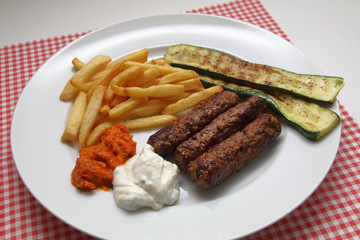 Cevapcici mit Pommes frites, Zucchini, Ajvar und Tzatziki.