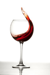 Red wine splashes out of a glass making waves in the glass
