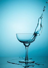 Water or alcohol splashes out of a glass making waves in the glass