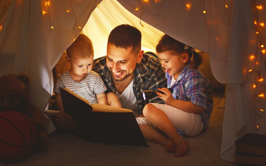 happy family father and children reading a book  in  tent at home