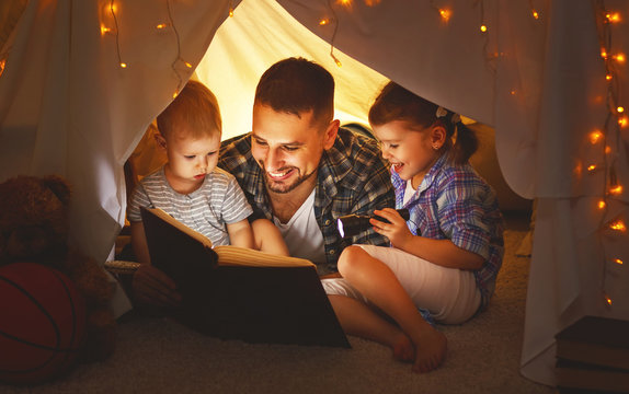 happy family father and children reading a book  in  tent at home