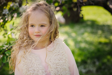 spring portrait of beautiful dreamy curly 5 years old child girl walking in blooming garden