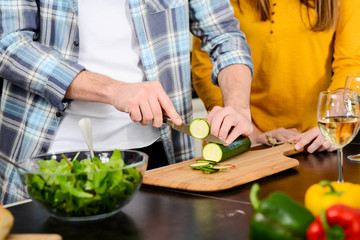 hands close-up group of friends, four people man and woman at home cooking, drinking wine and preparing food meal together in the kitchen