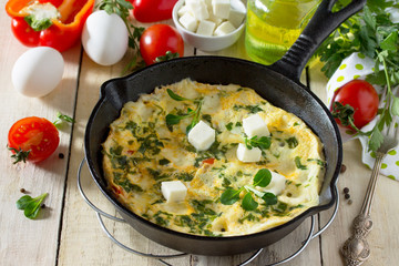 Omelette with peppers, tomatoes and feta cheese in a cast iron frying pan on a wooden table. The concept of healthy nutrition and diet. Bulgarian cuisine.