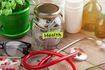 Saving money for health care insurance - money glass, stethoscope, pills and bottles