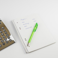 Ein Schreibblock  mit einer Berechnung der Ausgaben, ein grüner Stift und Taschenrechner, quadratisch