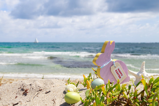 Rabbit shape with happy Easter tag and eggs on the sandy tropical beach back ground.