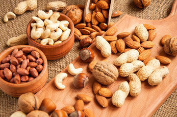 Almonds, cashew, walnuts and hazelnuts in wooden bowls on wooden and burlap, sack background