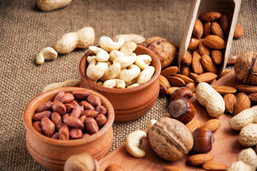 Almonds, cashew, walnuts and hazelnuts in wooden bowls on wooden and burlap, sack background