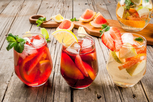 Traditional summer drink sangria - red, pink and white. With champagne, pink and red wine, strawberries, oranges, lemon, green apple and grapefruit. On a wooden rustic table, copy space 