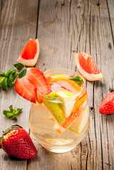 Traditional summer drink white sparkling sangria. With champagne, strawberries, oranges, lemon, green apple and grapefruit. On a wooden rustic table, with a jug and ingredients. Copy space