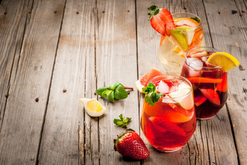 Traditional summer drink sangria - red, pink and white. With champagne, pink and red wine, strawberries, oranges, lemon, green apple and grapefruit. On a wooden rustic table, copy space 