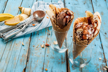 Two dessert banana split: chocolate and vanilla ice cream, with banana, waffle powder and nuts. On a light blue rustic wooden table copy space