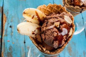 Dessert banana split: chocolate ice cream, with banana, waffle powder and nuts. On a light blue rustic wooden table close view copy space