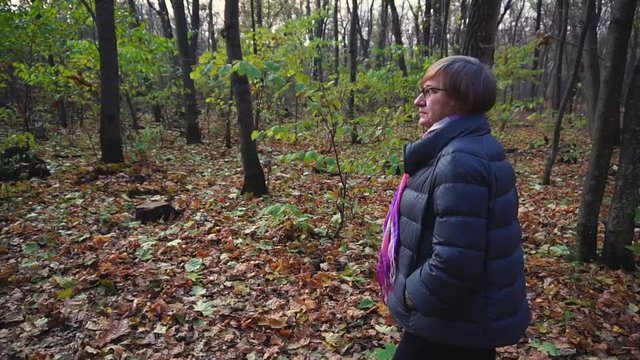 Senior woman walks in the autumn forest in a nice day.