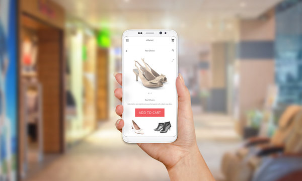Online shop on mobile phone display. Modern white smart phone with round edges in girl hand. Shopping mall in background.