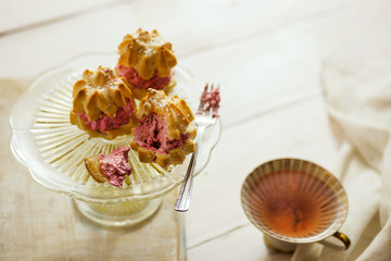 Strawberry cream puffs on a cake plate, served with tea. Shallow depth of field.