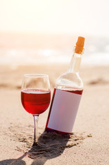 Glass of red rose wine and bottle on the beach at the summer sunny day. Sea on the background