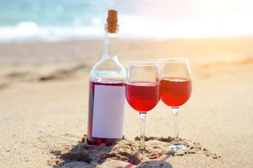 Glass of red rose wine and bottle on the beach at the summer sunny day. Sea on the background