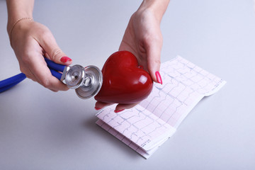 Female doctor hold in hands red toy heart and stethoscope. Cardio therapeutist, arrhythmia concept
