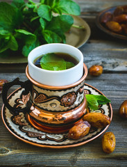 Tea with mint in arab style and dates on wooden table.