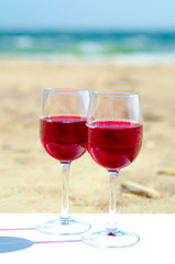 Romantic picnic with glasses of red rose wine on the beach at the summer sunny day. Sea on the background