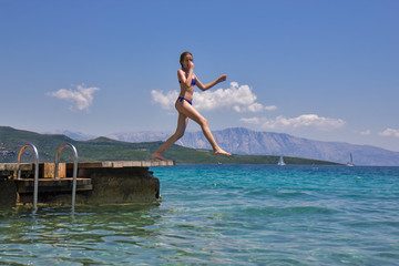 Girl jumping from a wooden pier in the sea
