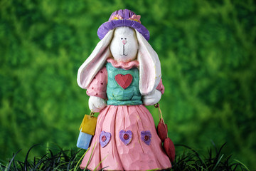 Obraz premium white female rabbit figurine wearing a purple hat and pink dress standing in green grass