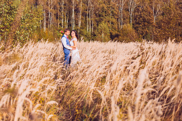 Naklejka na ściany i meble Wedding couple in love. Beautiful bride in white dress and handsome groom in black suite walking together in summer field.