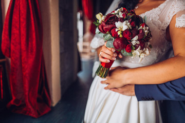 Beautiful pink red and Marsala Weding bouquet of different flowers in the hands of the bride in a white wedding dress. Bride with a wedding bouquet with peonies, callas, roses