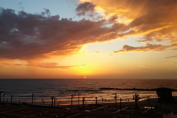 Fototapeta na wymiar Dramatic colored sky sunset above Haifa city coastline Mediterranean Sea, Israel. Silhouettes of people in the water and on the beach