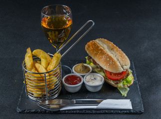 crusty white bread with sesame seeds, flavored with smoky ribsteak bbq, barbeque sauce, lettuce, tomato, three sauces, chips in a metal basket, white wine