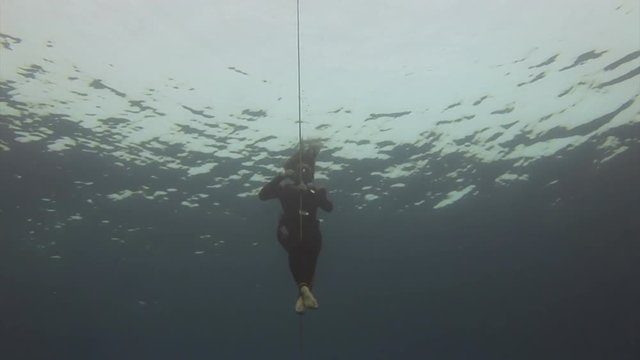 Underwater model free diver swims with red buoy in clean blue water in Red Sea. Filming a movie. Young girl smiling at camera. Extreme sport in marine landscape, coral reefs, ocean inhabitants.
