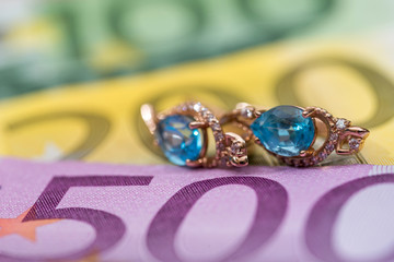 gold earrings lying on euros banknote.