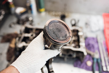 Car mechanic in garage with old car engine piston.