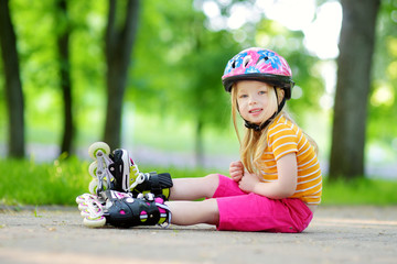 Pretty little girl learning to roller skate on beautiful summer day in a park